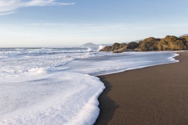 Nesika Sahili, Oregon 'daki Rocky kıyı şeridi. Öğleden sonra güneş ufka yaklaşırken dalgalar kayalara çarpıyor.