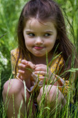 Porträt eines glücklichen vierjährigen Mädchens, das im grünen Gras sitzt