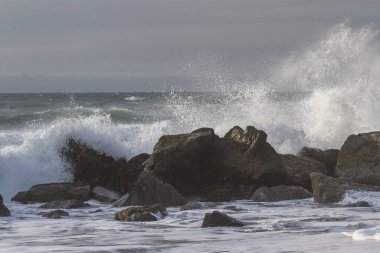 Nesika Sahili, Oregon 'daki Rocky kıyı şeridi. Öğleden sonra güneş ufka yaklaşırken dalgalar kayalara çarpıyor.