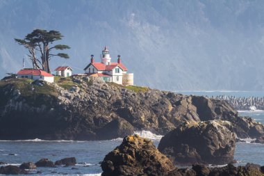 Crescent City California 'nın hemen dışındaki gelgit adasında Del Norte County' nin en çok ziyaret edilen yapılarından biri olan Battery Point Deniz Feneri 'nin arka plandaki karanlık dağlara karşı alçak gelgitte havada biraz sis görüldü..