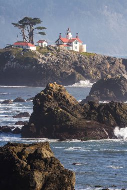 Crescent City California 'nın hemen dışındaki gelgit adasında Del Norte County' nin en çok ziyaret edilen yapılarından biri olan Battery Point Deniz Feneri 'nin arka plandaki karanlık dağlara karşı alçak gelgitte havada biraz sis görüldü..