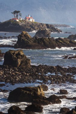 Crescent City California 'nın hemen dışındaki gelgit adasında Del Norte County' nin en çok ziyaret edilen yapılarından biri olan Battery Point Deniz Feneri 'nin arka plandaki karanlık dağlara karşı alçak gelgitte havada biraz sis görüldü..