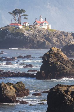 Crescent City California 'nın hemen dışındaki gelgit adasında Del Norte County' nin en çok ziyaret edilen yapılarından biri olan Battery Point Deniz Feneri 'nin arka plandaki karanlık dağlara karşı alçak gelgitte havada biraz sis görüldü..