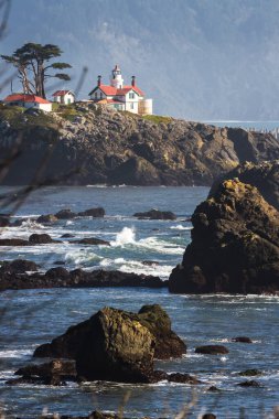 Crescent City California 'nın hemen dışındaki gelgit adasında Del Norte County' nin en çok ziyaret edilen yapılarından biri olan Battery Point Deniz Feneri 'nin arka plandaki karanlık dağlara karşı alçak gelgitte havada biraz sis görüldü..