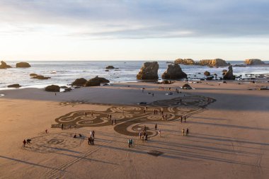 Bandon by the Sea, Oregon / USA - 08 Mart 2020: İnsanlar gün batımında Face Rock State Park plajında yürüyorlar Kum Çemberi ekibi tarafından oluşturulan bir labirentte