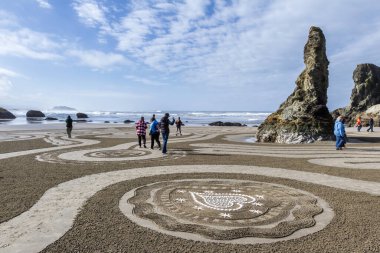 Bandon by the Sea, Oregon / USA - 13 Mart 2020: İnsanlar Kum Çemberi ekibi tarafından oluşturulan plajda labirentte inanılmaz detaylı sanat eserleriyle yürüyorlar
