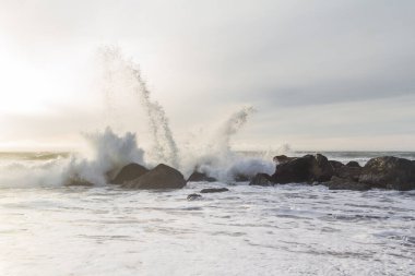 Nesika Sahili, Oregon 'daki Rocky kıyı şeridi. Öğleden sonra güneş ufka yaklaşırken dalgalar kayalara çarpıyor.