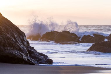 Nesika Sahili, Oregon 'daki Rocky kıyı şeridi. Öğleden sonra güneş ufka yaklaşırken dalgalar kayalara çarpıyor.