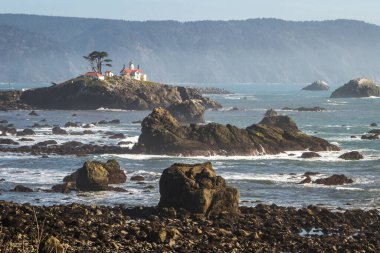 Crescent City California 'nın hemen dışındaki gelgit adasında Del Norte County' nin en çok ziyaret edilen yapılarından biri olan Battery Point Deniz Feneri 'nin arka plandaki karanlık dağlara karşı alçak gelgitte havada biraz sis görüldü..