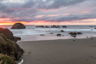 Günün sonunda plajda koyu bulutlarda biraz renk ve belirgin kaya karakteristik Face Rock State Park, Bandon Oregon