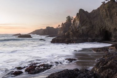 Gün batımında Güney Oregon sahilindeki gizli sahilde güneş batıyor. Dalgalar değiştikçe dalgalar bulanıklaşıyor.