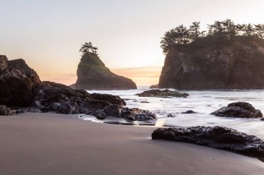 Gün batımında Güney Oregon sahilindeki gizli sahilde güneş batıyor. Dalgalar değiştikçe dalgalar bulanıklaşıyor.