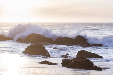 Nesika Sahili, Oregon 'daki Rocky kıyı şeridi. Öğleden sonra güneş ufka yaklaşırken dalgalar kayalara çarpıyor.