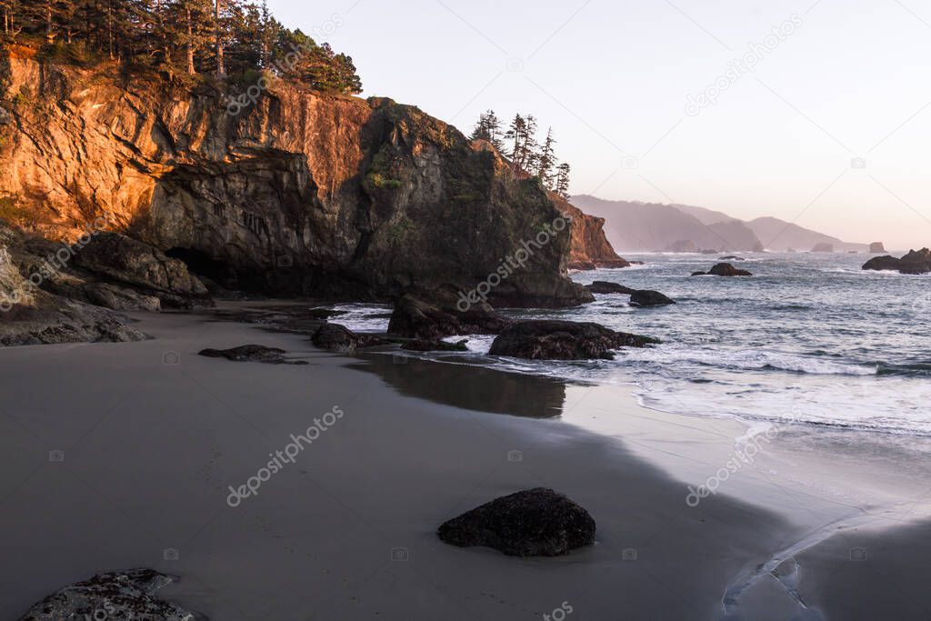 Beautiful sunset in Secret Beach Oregon with a soft warm glow on the rocks and evergreen trees on top of the islets that make this beach so recognizable.