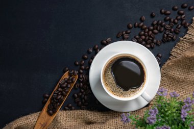  bir fincan kahve siyah masada. Üstten görünüm mockup bir fincan kahve kahve çekirdekleri ve kenevir torba siyah taş ile.