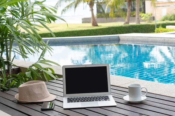 Dizüstü bilgisayar ve akıllı telefon ile kahve fincanı ve ahşap üzerine şapka. laptop ya da defter ve havuz başında şapka. 