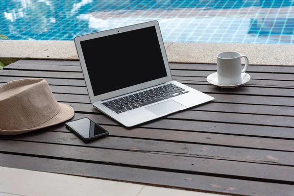 Dizüstü bilgisayar ve akıllı telefon ile kahve fincanı ve ahşap üzerine şapka. laptop ya da defter ve havuz başında şapka. 