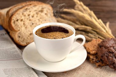 Sıcak kahve fincanı ve ahşap arka plan üzerinde pişmiş kahvaltı. Lezzetli kurabiyeleri, tahta arka plan ile lezzetli kahve fincan. Americano kahve ve kurabiye ile ekmek. Beyaz kahve fincanı.