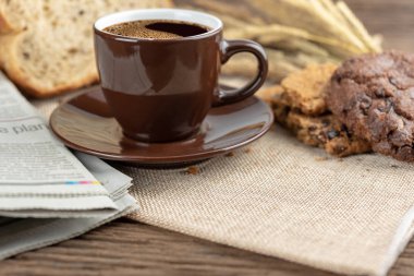 Sıcak kahve fincanı ve ahşap arka plan üzerinde pişmiş kahvaltı. Lezzetli kurabiyeleri, tahta arka plan ile lezzetli kahve fincan. Americano kahve ve kurabiye ile ekmek. Kahverengi kahve fincanı.