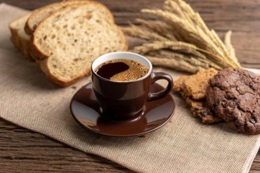 Sıcak kahve fincanı ve ahşap arka plan üzerinde pişmiş kahvaltı. Lezzetli kurabiyeleri, tahta arka plan ile lezzetli kahve fincan. Americano kahve ve kurabiye ile ekmek. Kahverengi kahve fincanı.