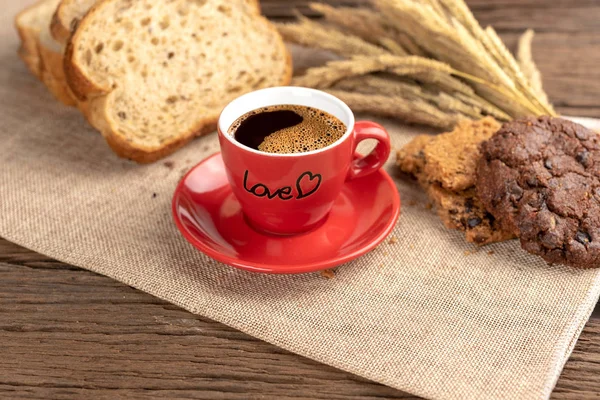 Sıcak kahve fincanı ve ahşap arka plan üzerinde pişmiş kahvaltı. Lezzetli kurabiyeleri, tahta arka plan ile lezzetli kahve fincan. Americano kahve ve kurabiye ile ekmek. Kırmızı kahve fincanı