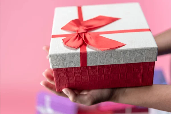 hands hold a empty red and white gift box on pink background for holiday, christmas, thanks giving day, birthday. Young woman hands holding red gift box.