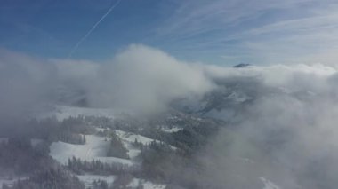 Binalar ile köy karla kaplı. Bulutların arasında havadan görünümü