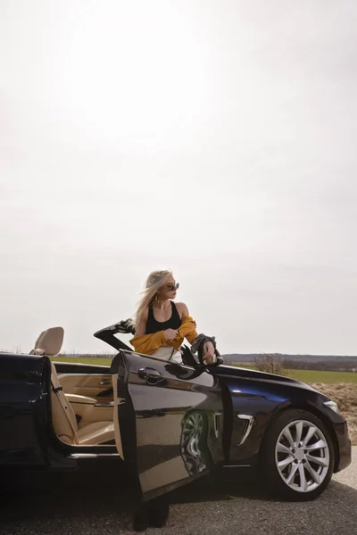 Atractiva joven posando apoyada en un coche descapotable — Foto de Stock