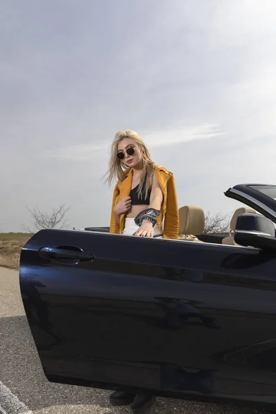 Attractive young woman posing leaning on convertible car