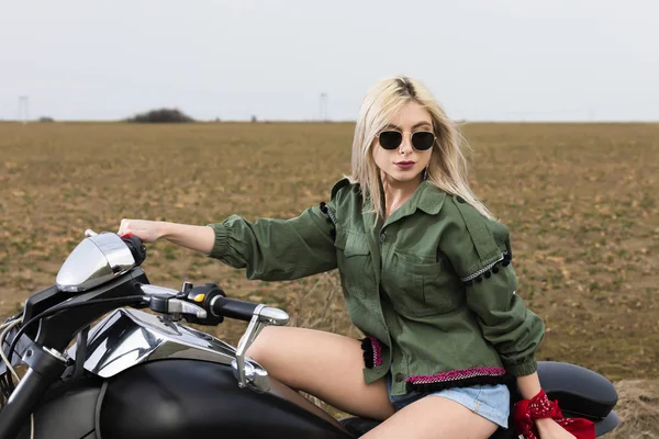 Uma bela jovem mulher sentada em uma moto preta e cromada — Fotografia de Stock