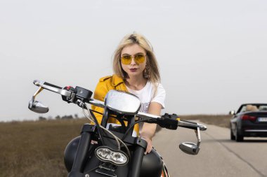 Güzel bir genç kadın siyah ve krom motosiklet üzerinde oturuyordu