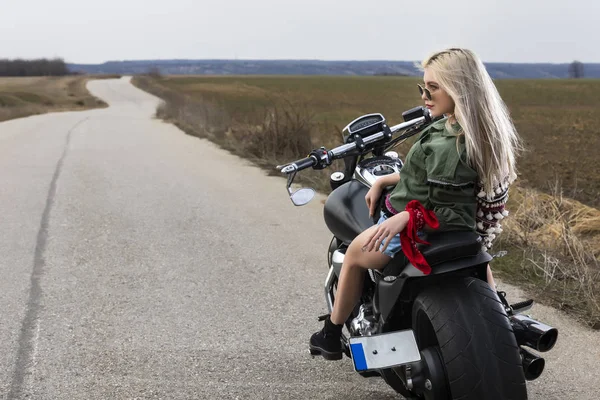 Uma bela jovem mulher sentada em uma moto preta e cromada — Fotografia de Stock