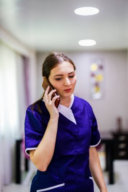 Temizlik servisi üniformalı kadın cep telefonu kullanıyor.