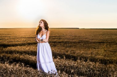 Gün batımında buğday tarlasında beyaz elbiseli güzel bir kadın..