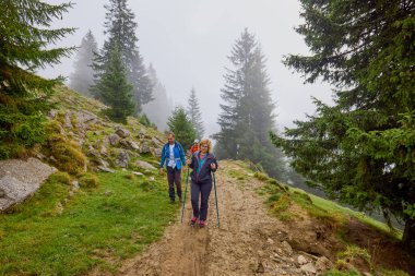 Bulutlu ve sisli bir günde büyükbabalarıyla dağlarda yürüyen bir çift..