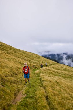 Bulutlu ve sisli bir günde büyükbabalarıyla dağlarda yürüyen bir çift..