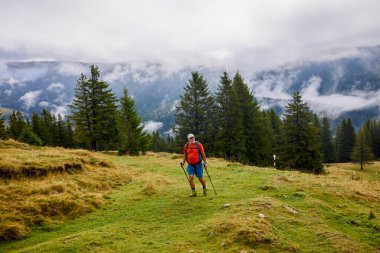 Güçlü yaşlı bir adam bulutlu bir günde dağa tırmanıyor.