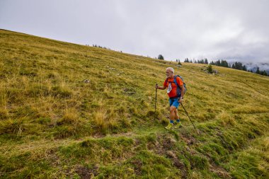 Güçlü yaşlı bir adam bulutlu bir günde dağa tırmanıyor.