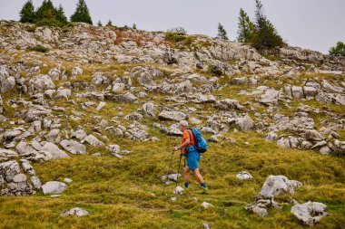 Güçlü yaşlı bir adam bulutlu bir günde dağa tırmanıyor.