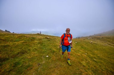 Güçlü yaşlı bir adam bulutlu bir günde dağa tırmanıyor.
