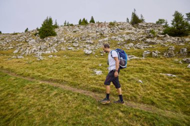Orta yaşlı bir adam bulutlu ve sisli bir günde dağa tırmanıyor.