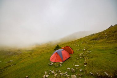 Sisli bir günde bir dağ manzarasında kamp kurmuş iki çadır.