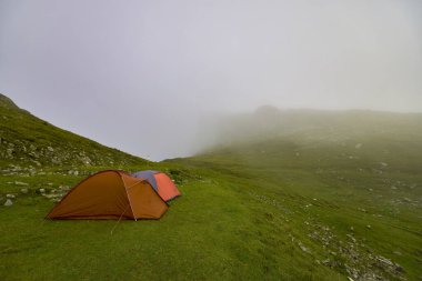 Sisli bir günde bir dağ manzarasında kamp kurmuş iki çadır.