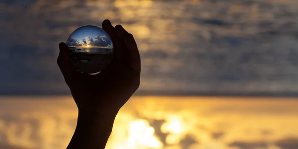 Crystal ball photography - sunset beach, hand holding the ball