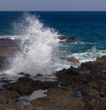 Gran Canaria, kuzey batı kıyısı doğal yüzme havuzları etrafında Salinas de Agaete, eski aşınmış karanlık lav platformuna karşı dalgalar kırılıyor.