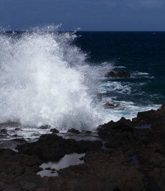 Gran Canaria, kuzey batı kıyısı doğal yüzme havuzları etrafında Salinas de Agaete, eski aşınmış karanlık lav platformuna karşı dalgalar kırılıyor.