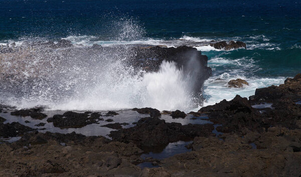 Gran Canaria, north west coast around natural swimming pools Salinas de Agaete, waves breaking against old eroded dark lava platform