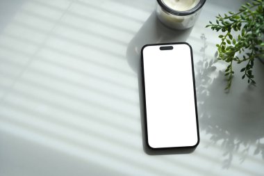Beyaz masaya yerleştirilmiş, bitki ve mumla süslenmiş, boş ekranlı akıllı telefon..