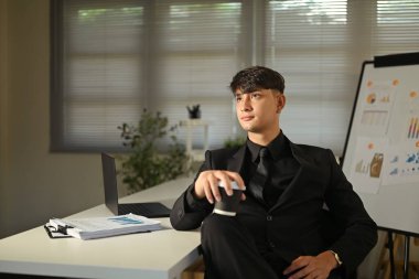 Girişimci resmi giysiler içinde elinde kahveyle düşünceli bir şekilde başını çeviriyor..