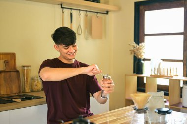 Genç beyaz bir adam mutfakta kahve öğütücüsüyle taze kahve çekirdeklerini öğütüyor..